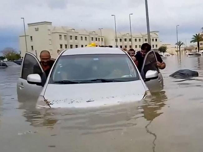 People push a stranded car along a flooded street in Dubai, Picture: AFP