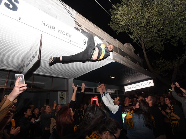 A Tigers supporter tries to climb on to a roof while celebrating along Swan St. Picture: AAP/James Ross