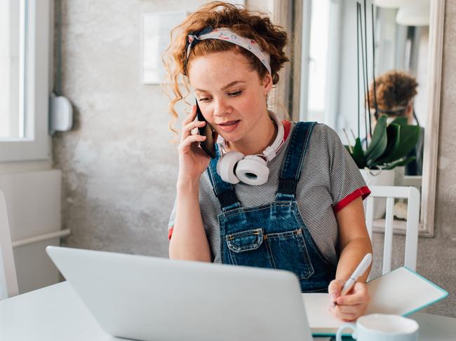 CORONAVIRUS:  Young woman working from her home office and talking on the phone during the quarantine due to Covid-19.