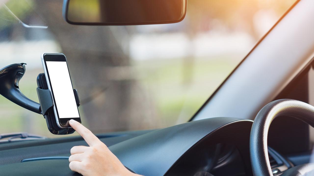 Hand touching a phone in a holder while driving a car. Picture: Supplied