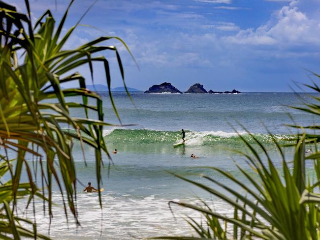 Surfers catching waves off Watgos Beach in Byron Bay with views across to Julian Rocks.Escape 4 June 2023Destinations - Byron IndigenousPhoto - Destination NSW