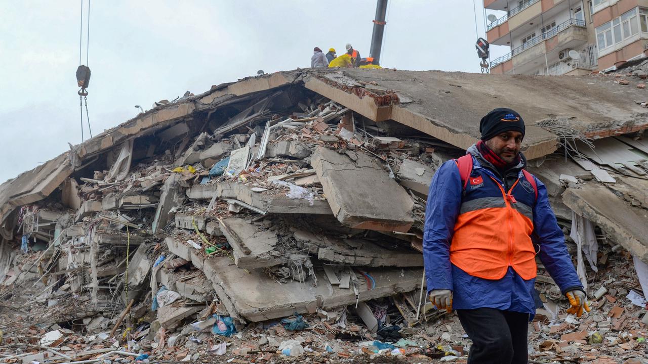 A man walks past a collapsed building as rescuers search for victims and survivors in Diyarbakir. (Photo by ILYAS AKENGIN / AFP)