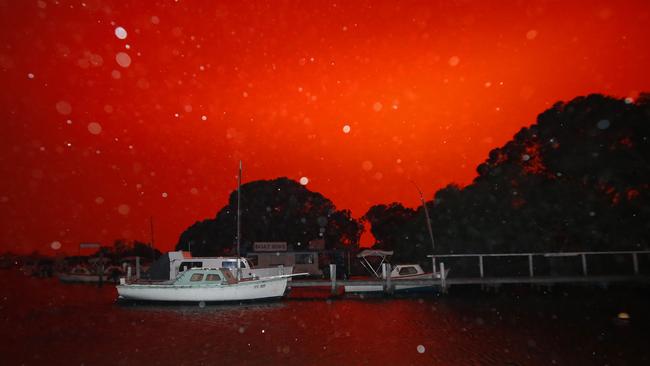 Ash falls over Mallacoota’s lake as the fires turn night to day. Picture: David Caird