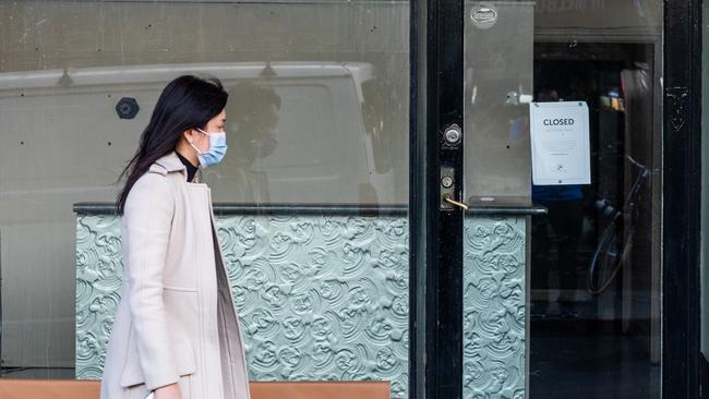 A woman wearing a mask walks past an empty store with a closed sign in the inner city suburb of Prahran in Melbourne today. Picture: Getty Images