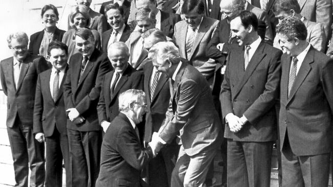 Aust politician Bill Hayden joking kneeling before Prime Minister Bob Hawke and members of ALP team when he arrived late for group photo session in 1987.