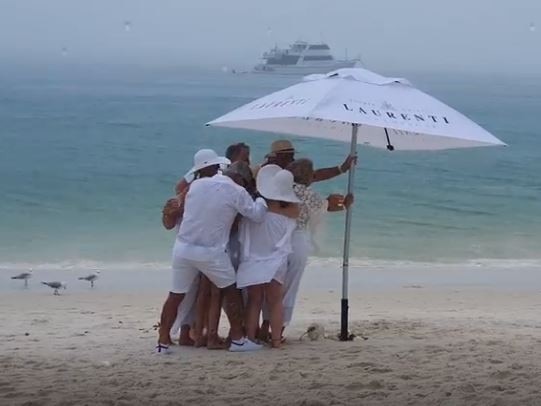 Revellers cling onto a beach umbrella as torrential rain smashes the White on Whitehaven Long Lunch.