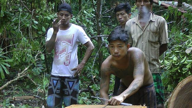 A former slave from Myanmar who goes by the name Mozet, centre, one of several slaves who escaped or ran away while Thai trawlers were docked at the Benjina port, cuts planks from a tree to earn money for food. Because the men were brought to Indonesia illegally — many after being tricked, sold or kidnapped by Thai brokers — they do not have any official documents and live in constant fear of being arrested.