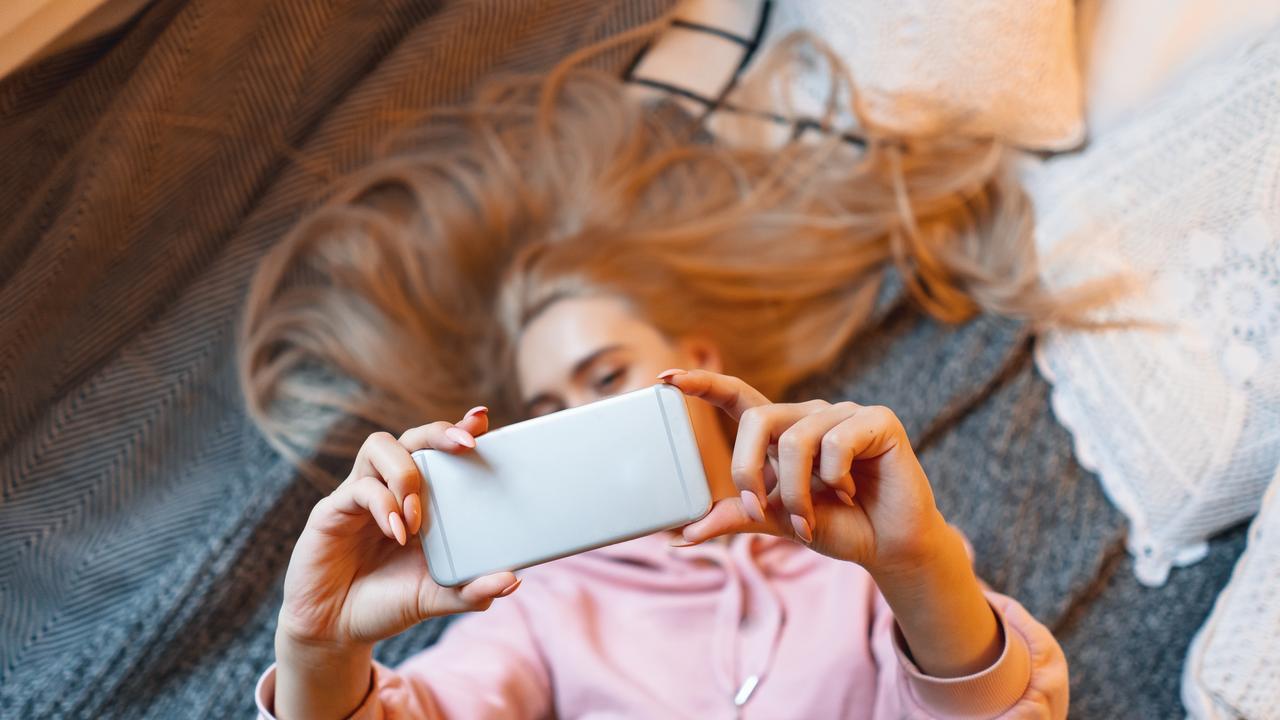 Pretty young girl having fun, making selfie while lying on the bed at home. Top angle view. Charming Caucasian woman taking picture of herself, for her friends and fans, for social media. Picture: Istock
