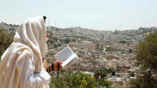 An Israeli settler from the Kiryat Arba Jewish settlement reads a holy book as he stands on Palestinian land overlooking the Ibrahimi Mosque and the old city of the West Bank town of Hebron. Picture: AFP.