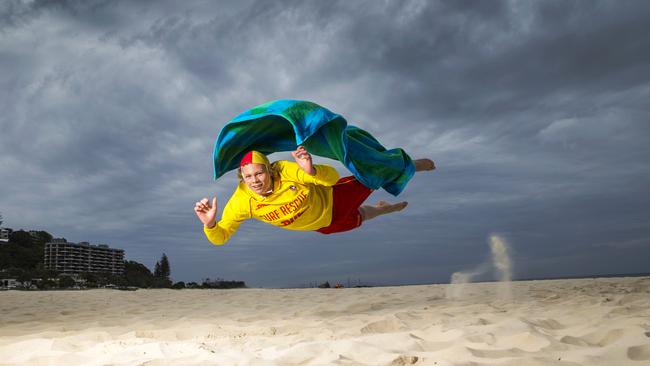 Currumbin lifesaver Darcy Winter plays super-hero on the beach with overcast skies and a gusty breeze. Picture: Nigel Hallett.