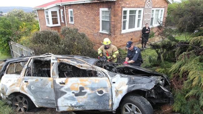 Tasmania Fire Service officers examining a car which caught fire after ploughing through a fence in the Launceston suburb of Newnham early today. Picture: BRUCE MOUNSTER