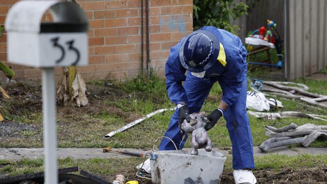 A forensic police officer picks up a teddy bear among the charred wreckage. Picture: Picture: Richard Dobson