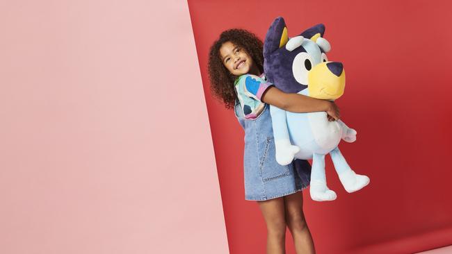 A child with a giant Bluey stuffed toy by Moose Toys.