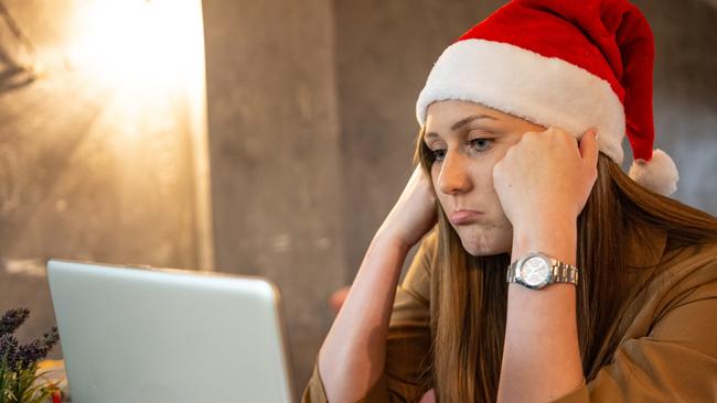 Young tired woman working on laptop wearing santa hat; Christmas spending debt generic