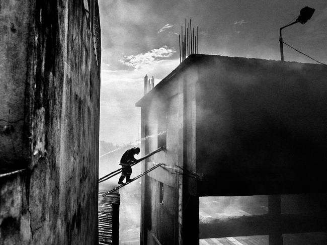 Tampaco Foils factory fire ... A firefighter is crossing from the nearer building’s roof to the affected building by using ladder to douse fire at ‘Tampaco Foils Limited’, a packaging factory at Tongi industrial area, Gazipur near to Dhaka, Bangladesh, September 10, 2016. Tampaco Foils Limited factory fire disaster, Bangladesh’s worst industrial disaster since the Rana Plaza collapse in 2013, left a total of 39 people dead and also injuring around 50. Flammable materials stored on the factory floor, a gas leak, excessive use of gas and poorly positioned boilers are all being looked at as possible reasons of the huge explosion and fire at the five-story factory building. Picture: Rahul Talukder, Bangladesh, 2nd Place, National Awards, 2017 Sony World Photography Awards