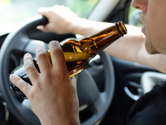 The concept of alcohol driving crime - closeup of young male driver hands with steering wheel and bottle of beer. Drink driving generic. Picture: iSTOCK