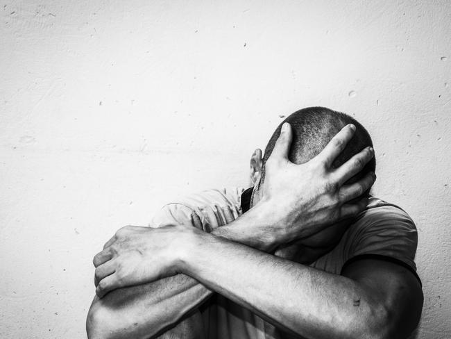 Homeless man drug and alcohol addict sitting alone and depressed on the street feeling anxious and lonely, social documentary concept black and white