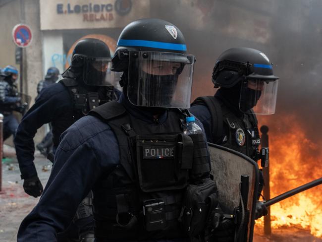 PARIS, FRANCE - MARCH 28: Police officers pass by a fire as they charge protesters during a rally against pension reforms on March 28, 2023 in Paris, France. The country has experienced weeks of protests and strike actions related to a rise in the pension age, which was passed last week. The 10th day of nationwide protests in France against the pension reforms are also calling out the police brutality from pervious strikes. (Photo by Carl Court/Getty Images)