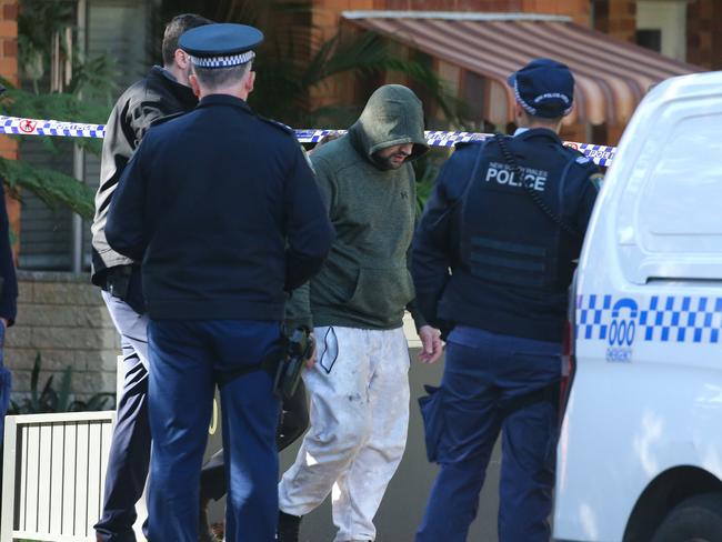 A man in a green hoodie is escorted from the premises by NSW Police to assist with their investigation.Picture: Newswire / Gaye Gerard