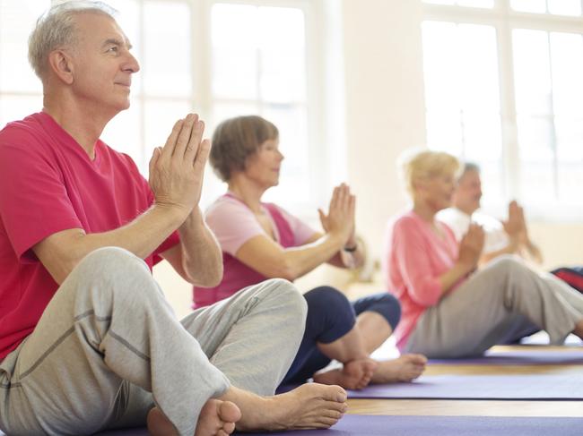 Senior man sitting in lotus position doing meditation with group of people in yoga class. For Good Life feature week 41.