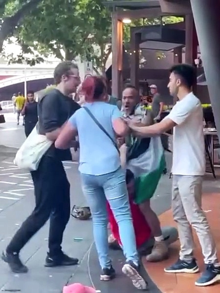 A man wearing a keffiyeh and holding a Palestinian flag is involved in an altercation with a man and woman in Southbank, Melbourne