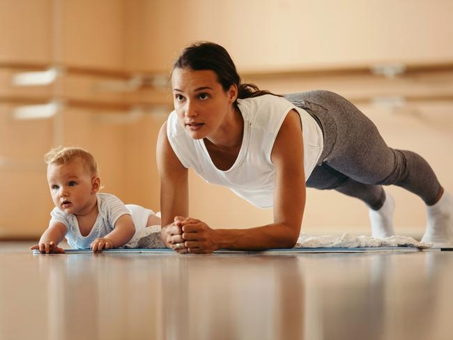 Athletic mother exercising in plank position while being with her baby in a health club. Copy space.