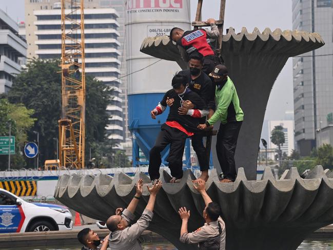 Police arrest a protester who climbed a fountain near the presidential palace during a protest by students against high prices of supplies, postponement of presidential elections and an extension of the President's term in Jakarta on April 11, 2022. (Photo by ADEK BERRY / AFP)