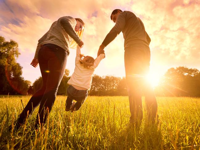 Happy family in the park evening light. The lights of a sun. Mom, dad and baby happy walk at sunset. The concept of a happy family.Parents hold the baby's hands.