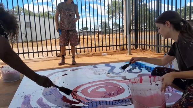 Stills taken from video where a non-indigenous employee is seen contributing to a painting by (Indigenous) artist Yaritji Young. The employee wearing darker clothing and holding a paint brush is Rosie Palmer, manager of Tjala Art in the settlement of Amata in the APY Lands.