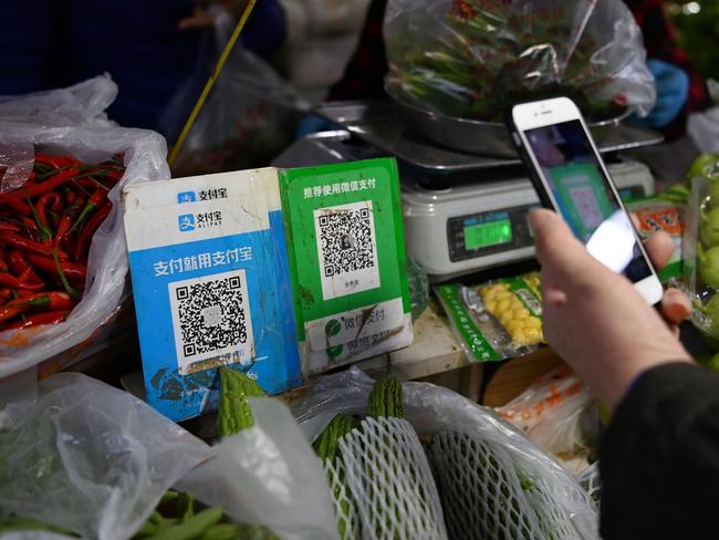 A customer makes a payment using a Wechat QR payment code (C) via her smartphone, next to an Alipay QR code (L), at a vegetable market in Beijing on November 3, 2020. (Photo by GREG BAKER / AFP)