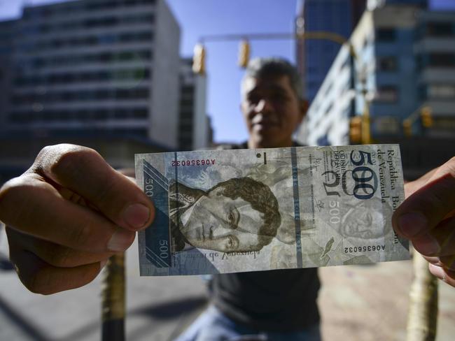 A street coffee vendor shows a new 500-Bolivar-note (74 cents of US dollar) in Caracas on January 16, 2017. The new 500-Bolivar-note is the first of a new family of currency that will progressively come into circulation. The South American country also has the highest inflation rate in the world, which IMF forecasts say could soon hit 475 percent. / AFP PHOTO / JUAN BARRETO