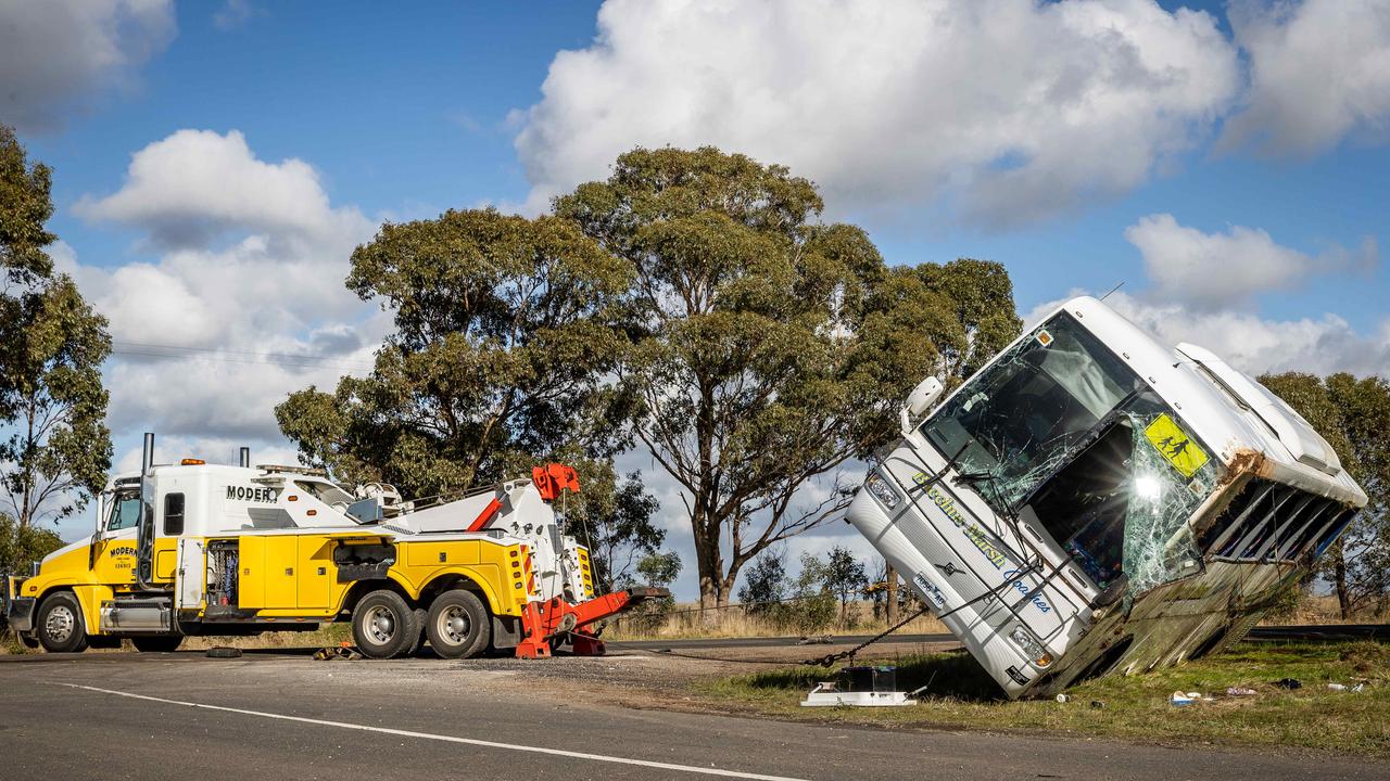 Crash scene investigators work at the scene while emergency services pick up school bags after the bus is pulled back onto its wheels. Picture: Jake Nowakowski