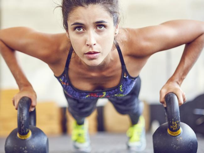 Focused athlete doing push-ups on kettlebells. Female is exercising in gym. Sporty woman is in health club.