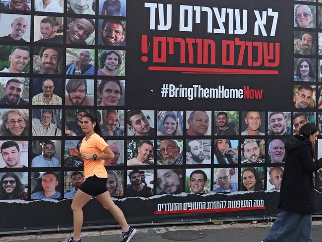 TOPSHOT - People walk past a billboard bearing the portraits of Israeli hostages, held in the Gaza Strip since the October 7, 2023 attacks by Hamas militants, in Jerusalem on February 17, 2025, as the country marks the 500th day since their abduction. (Photo by AHMAD GHARABLI / AFP)