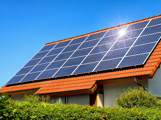 Developing Queensland - Solar panel on a red roof reflecting the sun and the cloudless blue sky.