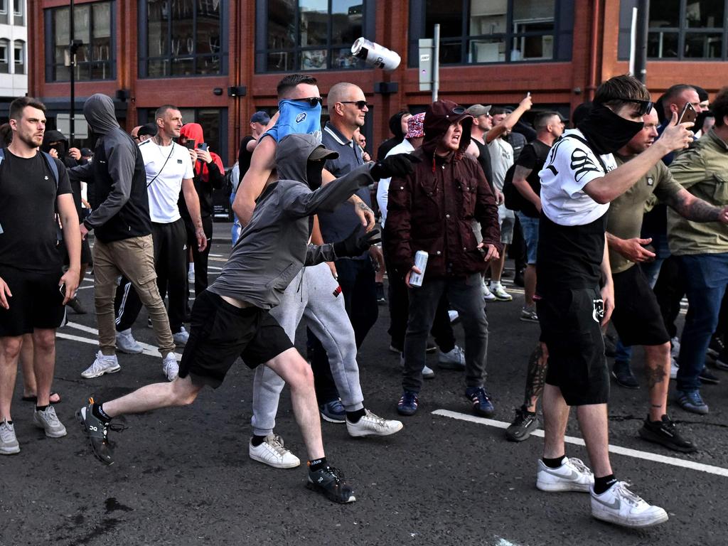 A masked protester throws a can of beer towards riot police in Bristol, southern England, on August 3, 2024 during the 'Enough is Enough' demonstration held in reaction to the fatal stabbings in Southport on July 29. UK police prepared for planned far-right protests and other demonstrations this weekend, after two nights of unrest in several English towns and cities following a mass stabbing that killed three young girls. (Photo by JUSTIN TALLIS / AFP)