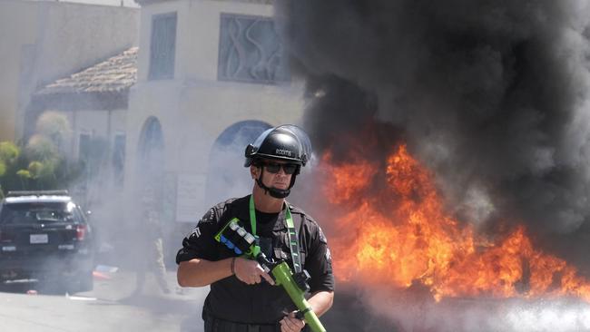 A police officer stands guard while a police vehicle burns in LA.