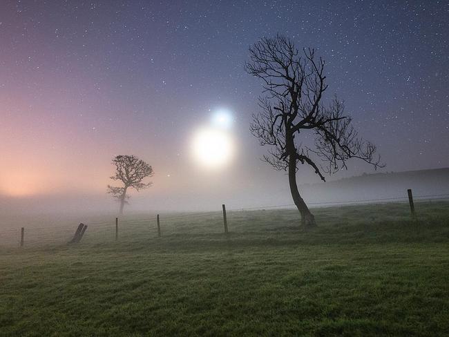 Binary Haze ... A misty morning in October on the Isle of Wight is the setting for this image resembling an eerie scene from a science fiction film. The obscuring weather actually accentuated the brightness of Venus and the crescent Moon and transformed them to appear as glowing orbs floating over the Ashey countryside. Picture: Ainsley Bennett, Insight Astronomy Photographer of the Year 2016 Skyscapes Winner