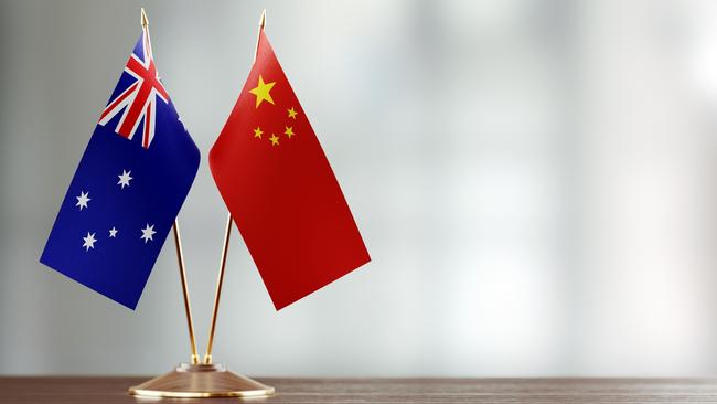 Australian and Chinese flag pair on desk over defocused background. Horizontal composition with copy space and selective focus.