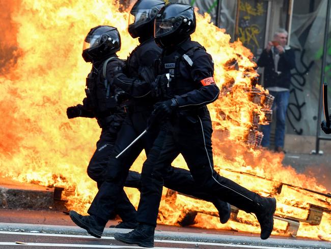 TOPSHOT - French riot police run past a fire during a demonstration in Paris on March 23, 2023, a week after the government pushed a pensions reform through parliament without a vote, using the article 49.3 of the constitution. - French unions on March 23, 2023, staged a new day of disruption against President Emmanuel Macron's pension reform after he defiantly vowed to implement the change, with refineries at a standstill and mass transport cancellations. (Photo by Alain JOCARD / AFP)