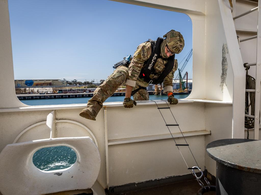 An officer scales a ladder to enter the ship to respond to a staged attack. Picture: Jake Nowakowski