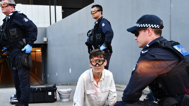 A woman glues herself to a car park entrance driveway. Picture: Jake Nowakowski