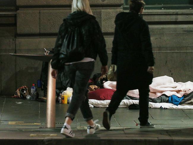 Pedestrians pass by as a man sleeps on the path in Flinders Street. Picture: Ian Currie