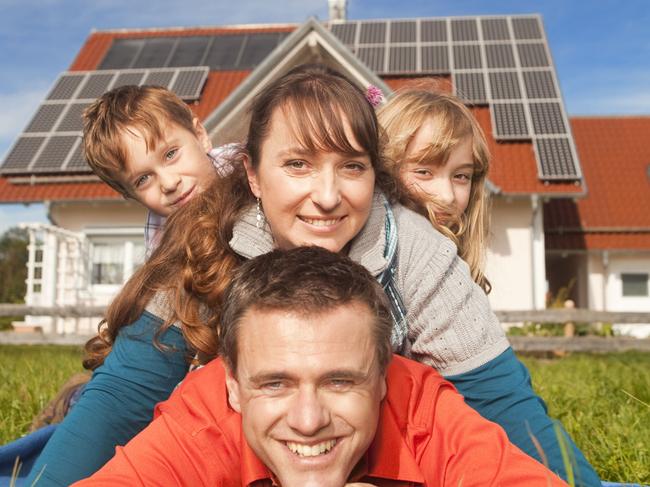 Happy family lying in grass in front of house with solar panels.