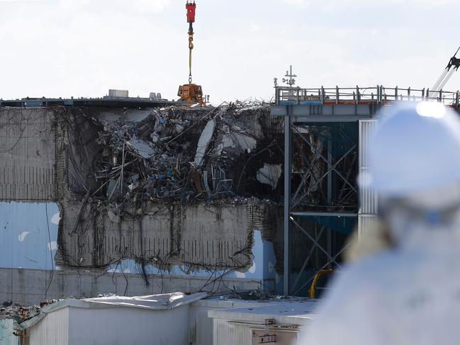 (FILES) This file photo taken on February 10, 2016 shows a member of the media, wearing a protective suit and a mask, looking at the No. 3 reactor building during a press tour at Tokyo Electric Power Co's (TEPCO) tsunami-crippled Fukushima Daiichi nuclear power plant in the town of Okuma, Fukushima prefecture. Tokyo Electric power (TEPCO), the operator of Fukushima Daiichi plant in northeastern Japan, announced on August 31, 2017 that it will begin to extract the molten fuel from the reactors starting in 2021. / AFP PHOTO / POOL / TORU HANAI