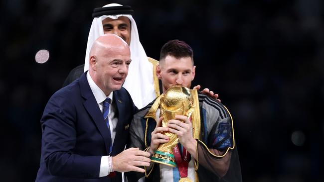 Lionel Messi of Argentina kisses the FIFA World Cup Winner's Trophy as Gianni Infantino, President of FIFA, and Sheikh Tamim bin Hamad Al Thani, Emir of Qatar, look on. (Photo by Julian Finney/Getty Images)