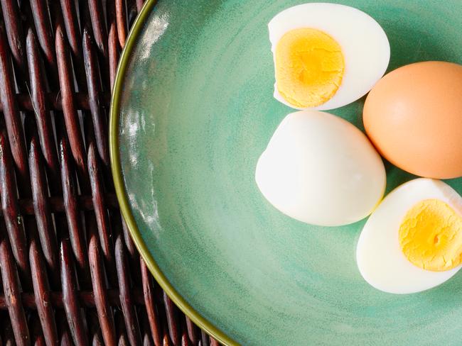 Hard-boiled egg cut and piled on egg slicer and full egg with shell on green plate or dish.