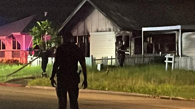 A police officer watches over the scene at a house fire in Ramsay St, Garbutt, which was under control before 9pm.