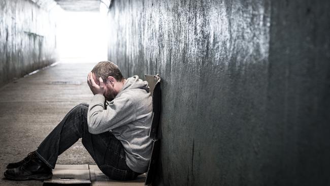 Young homeless male of caucasian ethnicity sitting on the floor of a dark subway tunnel with his hands on his head. Desaturated horizontal colour image with lots of room for copy space. LEV pg 8-9homeless man tunnel 2 iSTOCK