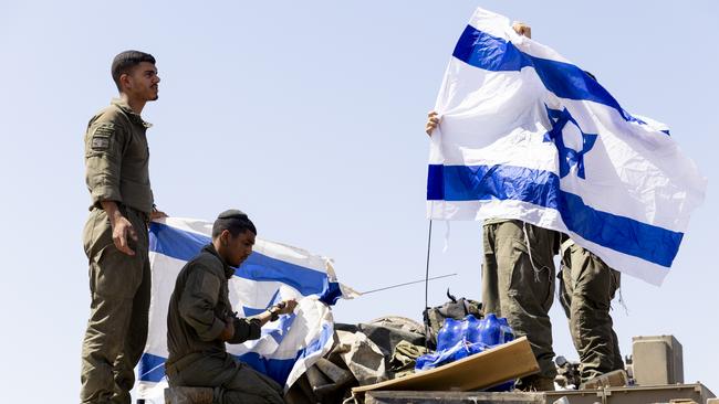 Israeli soldiers hang Israeli flags on an armoured personnel carrier near the border with the Gaza Strip. Picture: Getty Images.